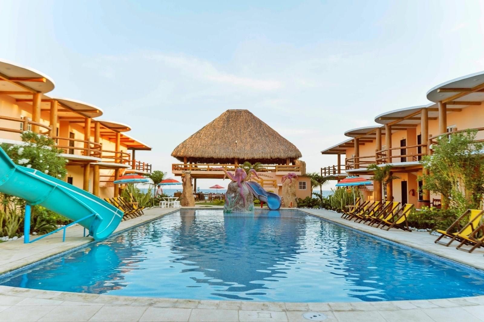 Piscina del Hotel Pazifico con toboganes, palapa central y el océano al fondo.